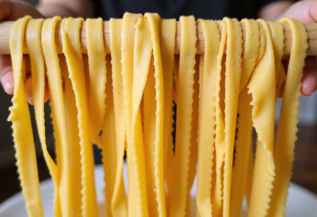 Homemade fettuccine pasta drying on a rack, made with a KitchenAid mixer.