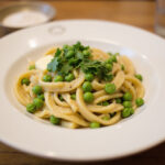 Homemade pasta and peas served in a bowl, garnished with parsley.