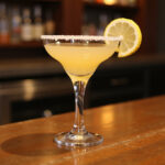 Finished lemon drop shot with lemon garnish on a bar top.