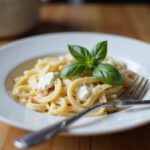 Bowl of cream cheese pasta garnished with basil, ready to eat.