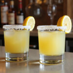Finished lemon drop shots garnished with lemon wedges on a bar.