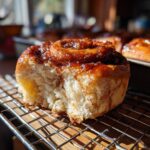 Close-up of a freshly baked apple butter cinnamon roll on a wire rack, showing its soft texture and glaze.