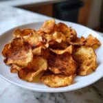 A plate piled high with golden-brown baked cinnamon apple chips, ready to eat.