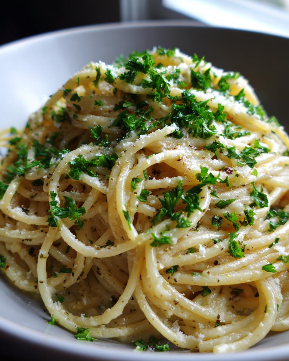 Close-up of creamy pasta dishes, topped with fresh parsley and parmesan cheese in a grey bowl.