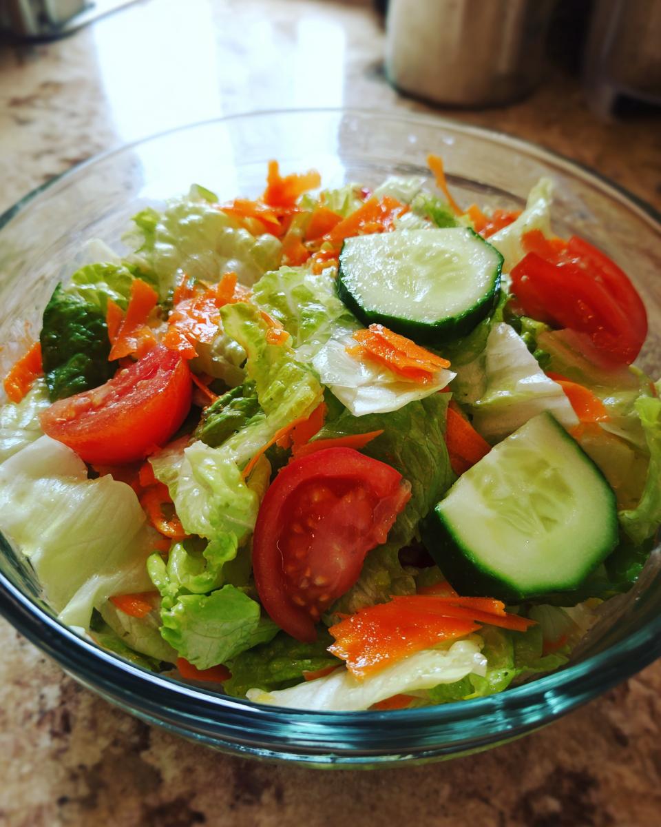 Close-up of a colorful easy salad recipes in a clear glass bowl, featuring lettuce, tomatoes, cucumber, and carrots.