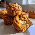 A stack of pumpkin cream cheese muffins, one muffin cut open to reveal the cream cheese filling.