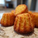 Close-up of golden brown Snoopy madeleines stacked on a marble surface, showcasing their unique shape.