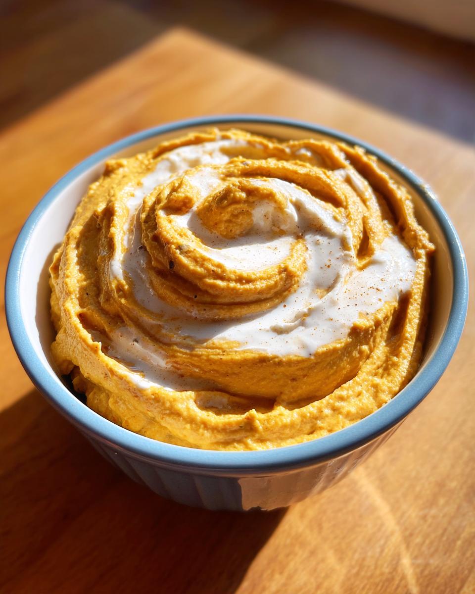 A bowl of Whipped Feta Pumpkin Hummus Swirl, featuring a creamy texture and a swirl of whipped feta on top.