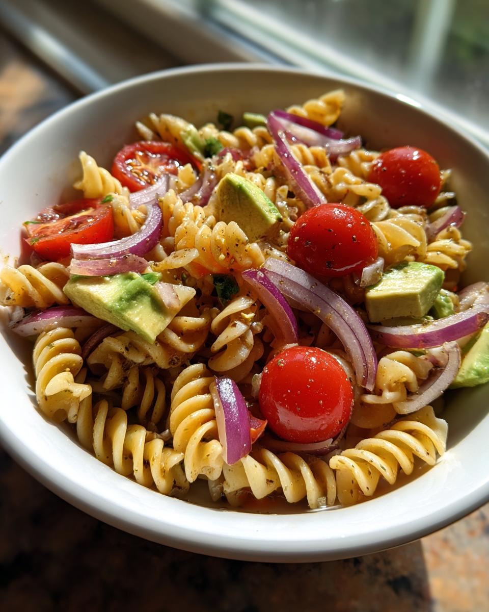 A vibrant bowl of 5-minute cooking aesthetic pasta salad with fusilli, cherry tomatoes, avocado, and red onion.