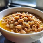 A close-up of a white bowl filled with a delicious black eyed peas recipe, showing the tender beans in a savory broth.