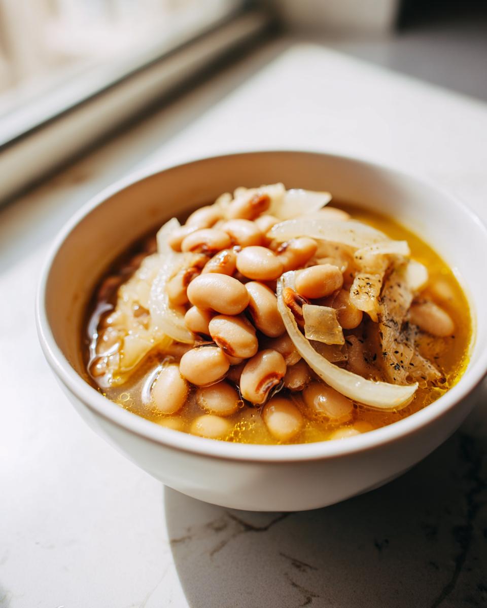 Close-up of a white bowl filled with a soulful black eyed peas recipe, featuring tender beans and sliced onions in a savory broth.