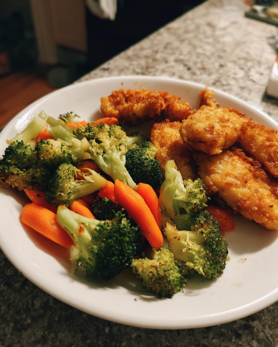 A plate of crispy chicken tenders served with steamed broccoli and carrots, perfect for easy weeknight dinners.