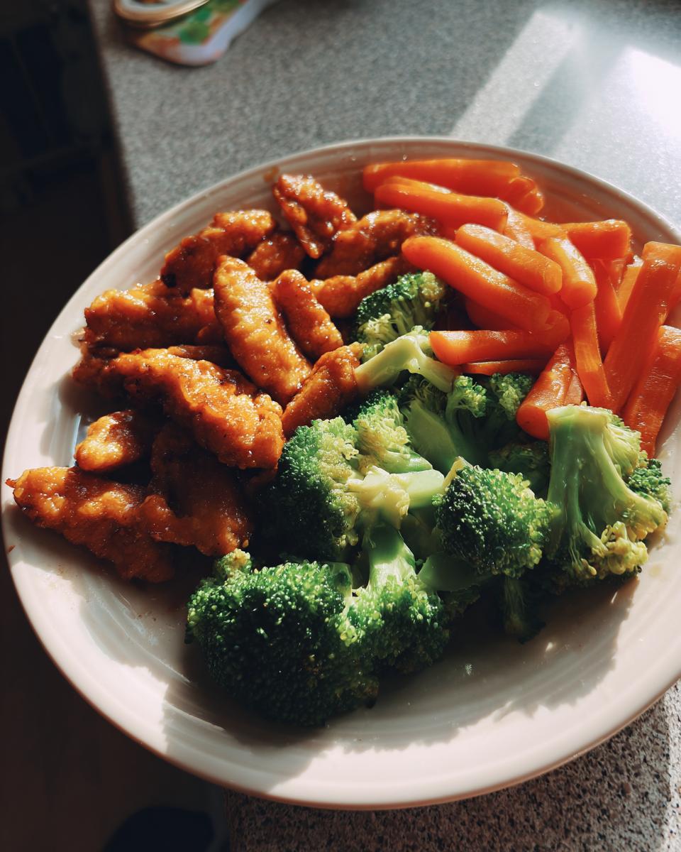 A plate of crispy chicken tenders with steamed broccoli and carrots, perfect for easy weeknight dinners.