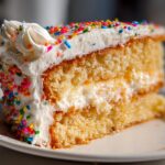 A slice of funfetti cake with white frosting and colorful sprinkles, perfect for New Years desserts.