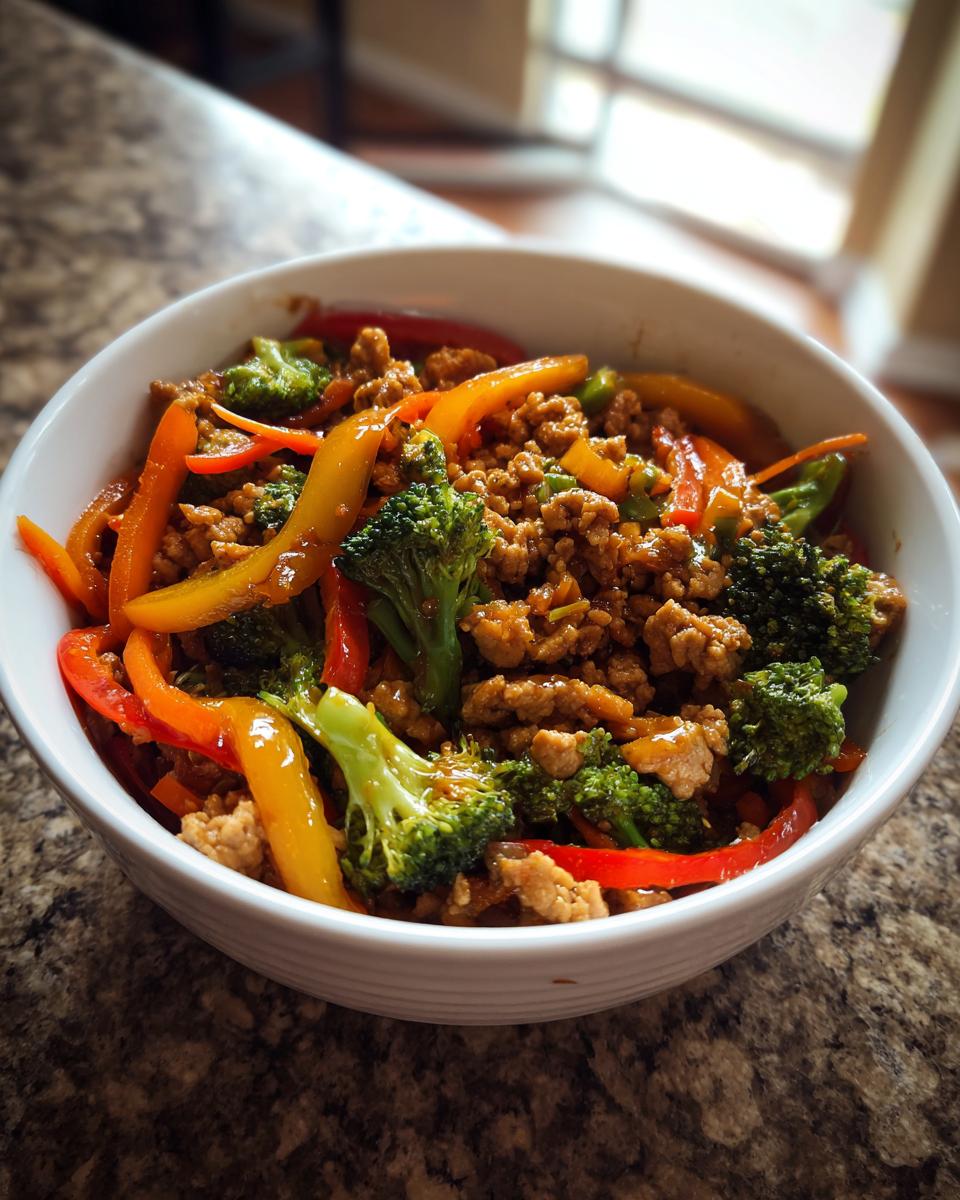 A white bowl filled with a colorful ground turkey stir fry, featuring broccoli florets and sliced bell peppers.