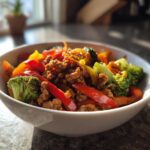 A white bowl filled with a colorful ground turkey stir fry, featuring broccoli florets, red and yellow bell peppers, and savory ground turkey.