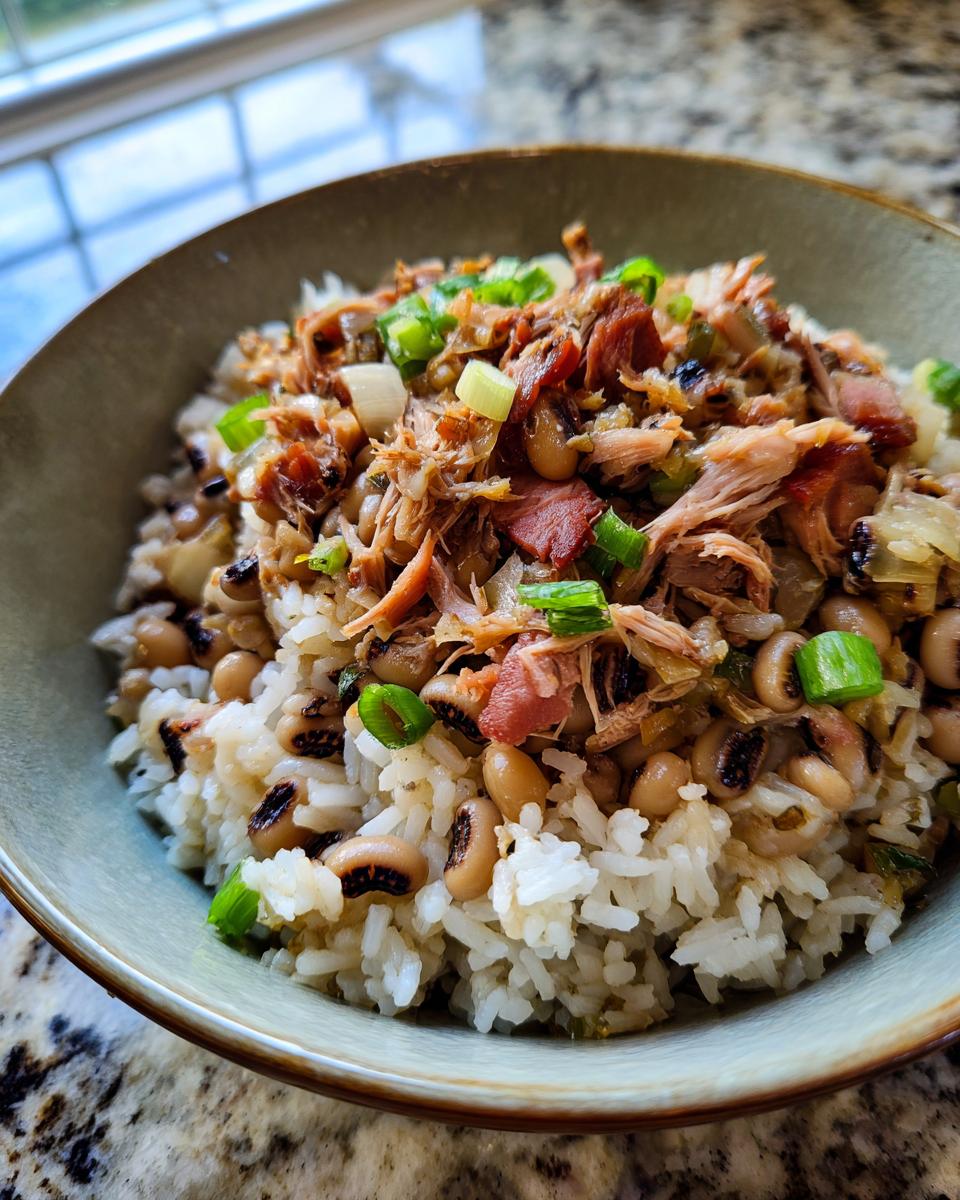 A close-up bowl of Hoppin John recipe with rice, black-eyed peas, pulled pork, and green onions.