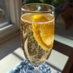 A close-up of a sparkling new years cocktail in a tall glass, garnished with a lemon slice and full of bubbles.