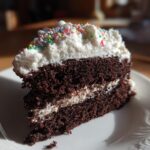A slice of rich chocolate cake with white frosting and colorful sprinkles, perfect for a New Years Eve dessert.