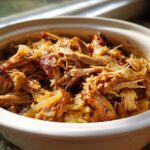Close-up of shredded pork and sauerkraut in a crockpot, glistening with juices.