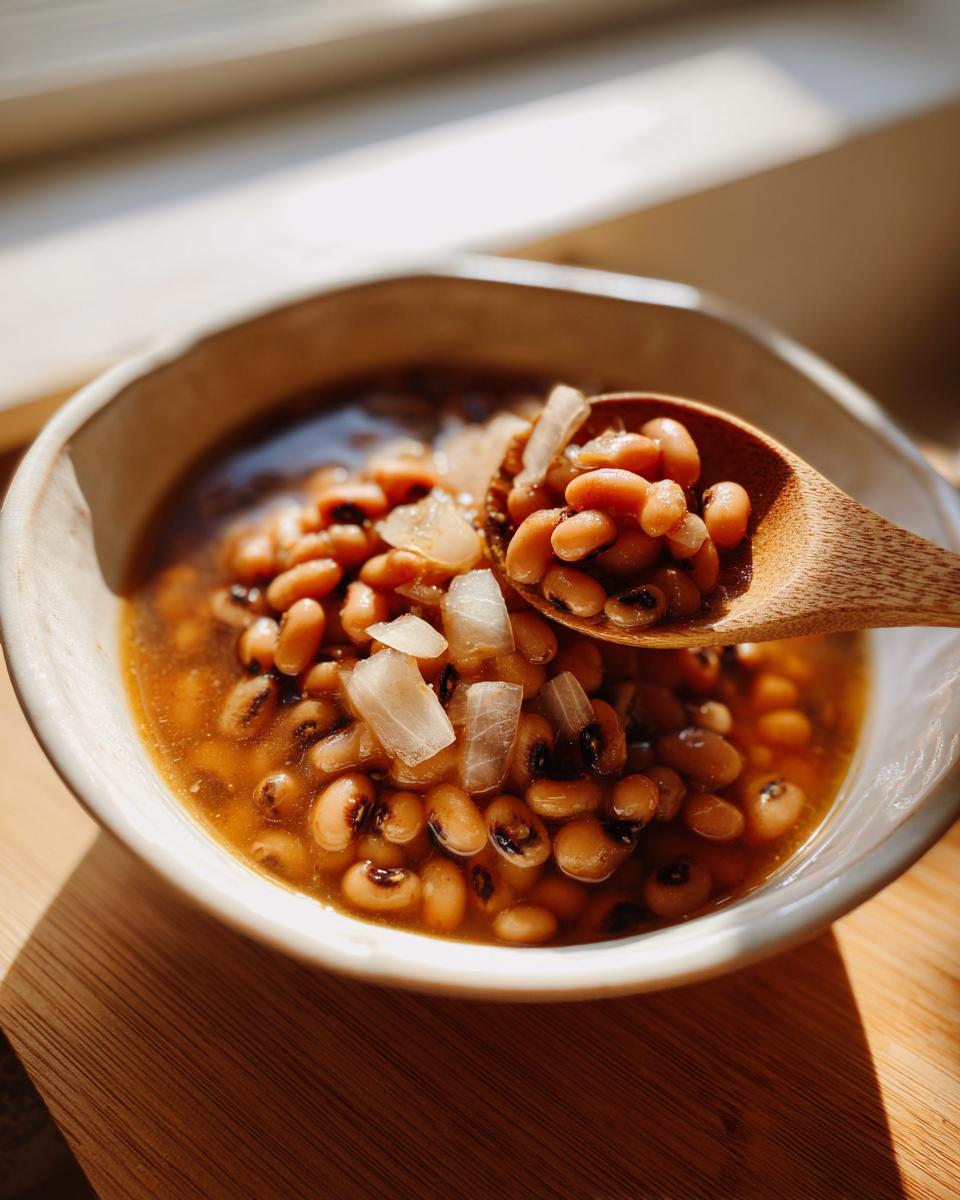 A close-up of a wooden spoon lifting a portion of Southern-style black eyed peas from a rustic bowl.