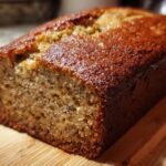 Close-up of a moist 3-ingredient banana bread loaf on a wooden cutting board.