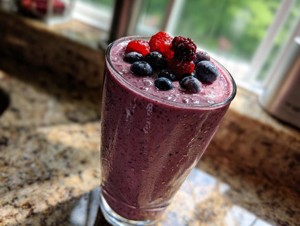 A tall glass of banana berry smoothie topped with fresh blueberries, raspberries, and blackberries.