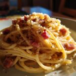 A close-up of a plate of spaghetti carbonara, a classic pasta recipe, topped with pancetta and black pepper.