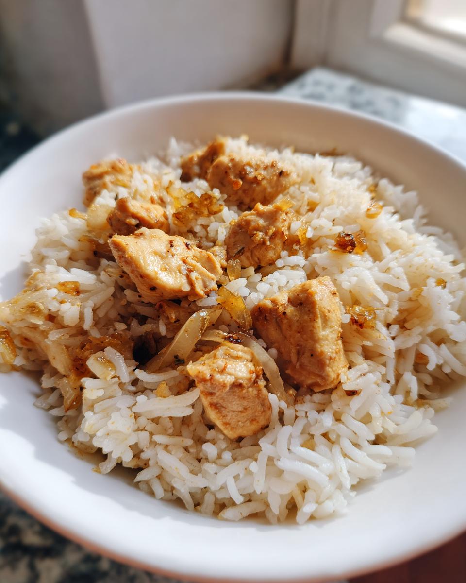 A close-up of a white bowl filled with fluffy white rice and seasoned chicken pieces, part of a delicious chicken and rice recipe.