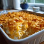 A spoonful of creamy chicken casserole with a crunchy cereal and cheese topping, served from a white baking dish.