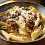 Close-up of creamy chicken pasta with penne noodles, seasoned chicken pieces, and grated cheese.