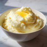 A close-up of a bowl filled with fluffy mashed potatoes topped with a melting pat of butter. This is one of the best mashed potatoes recipes.