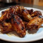 A close-up of a pile of perfectly baked crispy chicken wings, glistening with sauce on a white plate.
