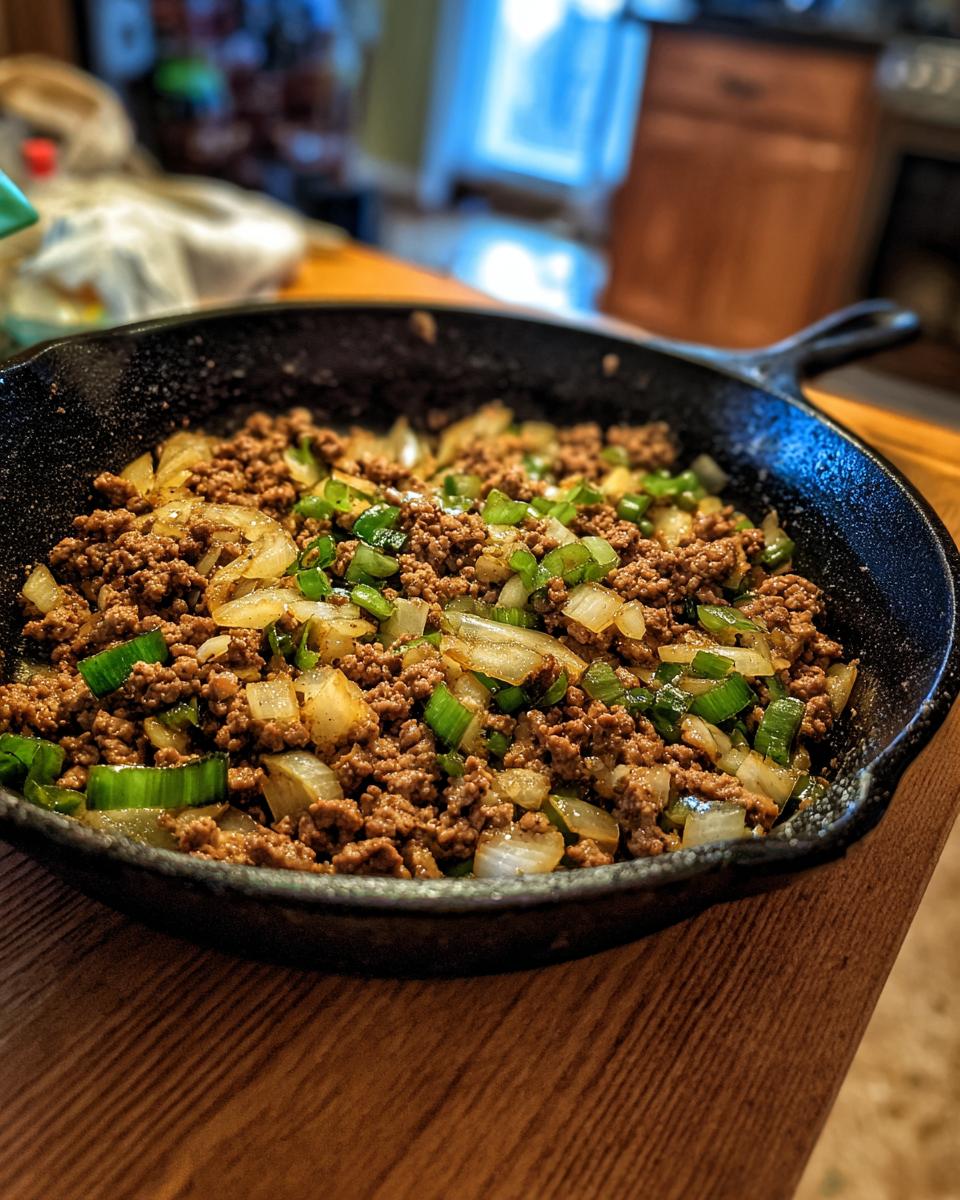 Ground turkey cooking with onions and green peppers in a cast iron skillet.