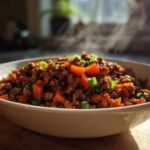 A close-up of a white bowl filled with steaming ground turkey and diced vegetables, garnished with green onions.