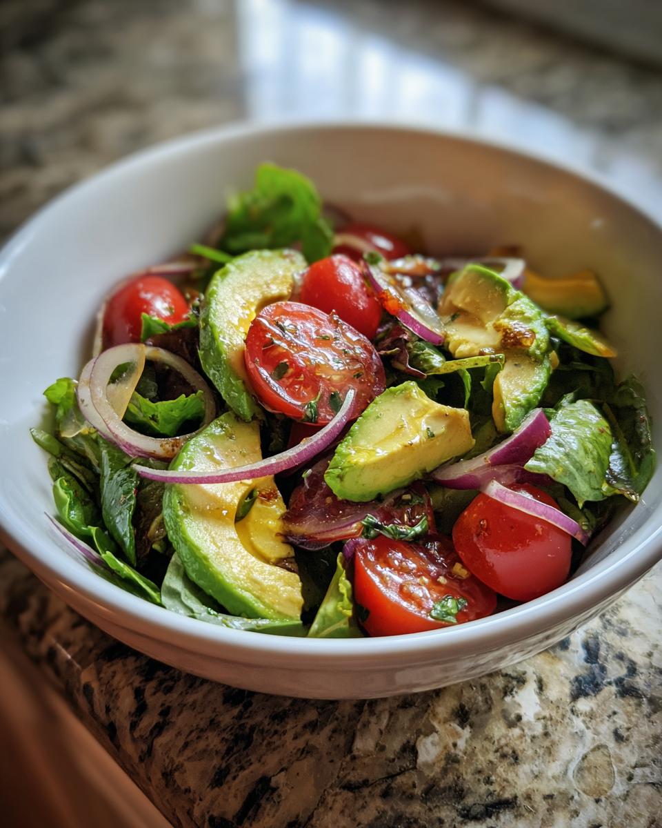 A refreshing bowl of healthy lunch ideas featuring avocado, cherry tomatoes, red onion, and mixed greens.