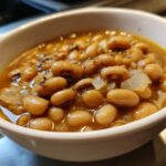 Close-up of a white bowl filled with a hearty black eyed peas recipe, featuring tender beans and onions in a savory broth.
