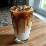 Close-up of a tall glass filled with ice, milk, espresso, and caramel drizzle, representing homemade Starbucks drinks.
