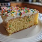 A slice of yellow cake with white frosting and colorful sprinkles, perfect for new years desserts.