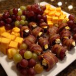 A platter of delicious new years eve appetizers featuring bacon-wrapped dates, cheese cubes, and fresh grapes.