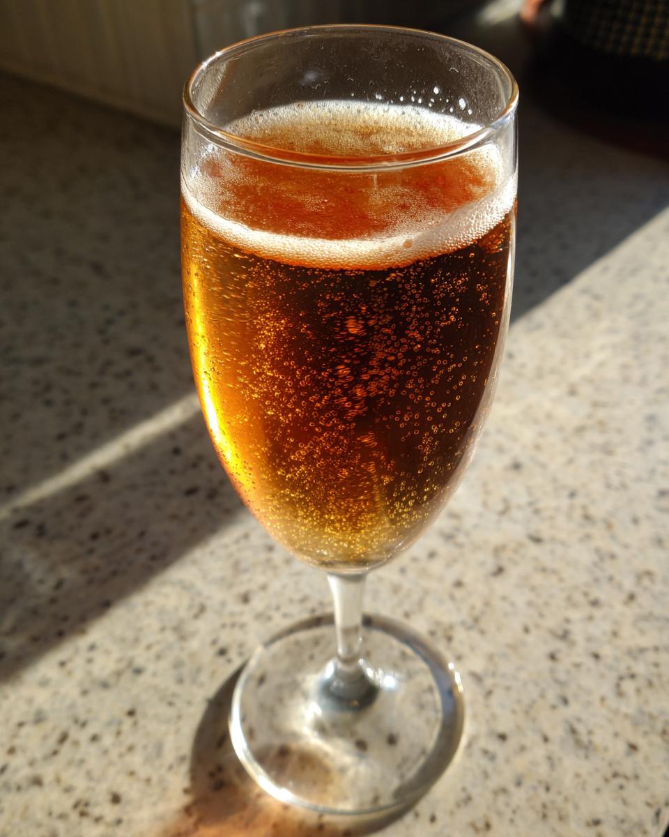 A close-up of a bubbly, amber-colored NYE cocktail in a champagne flute, ready for a New Year's toast.