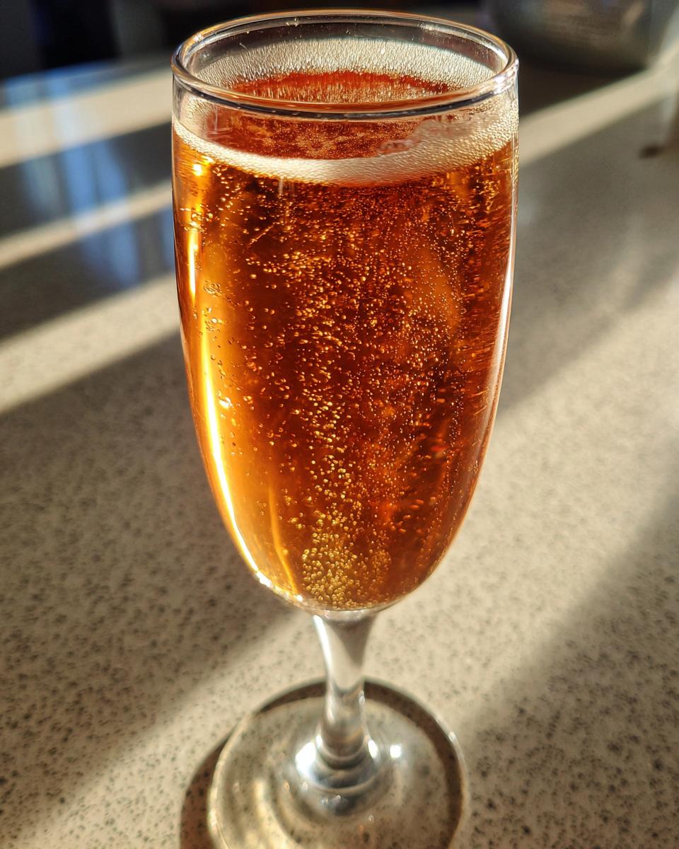 A close-up of a bubbly, amber-colored NYE cocktail in a champagne flute, catching the light.