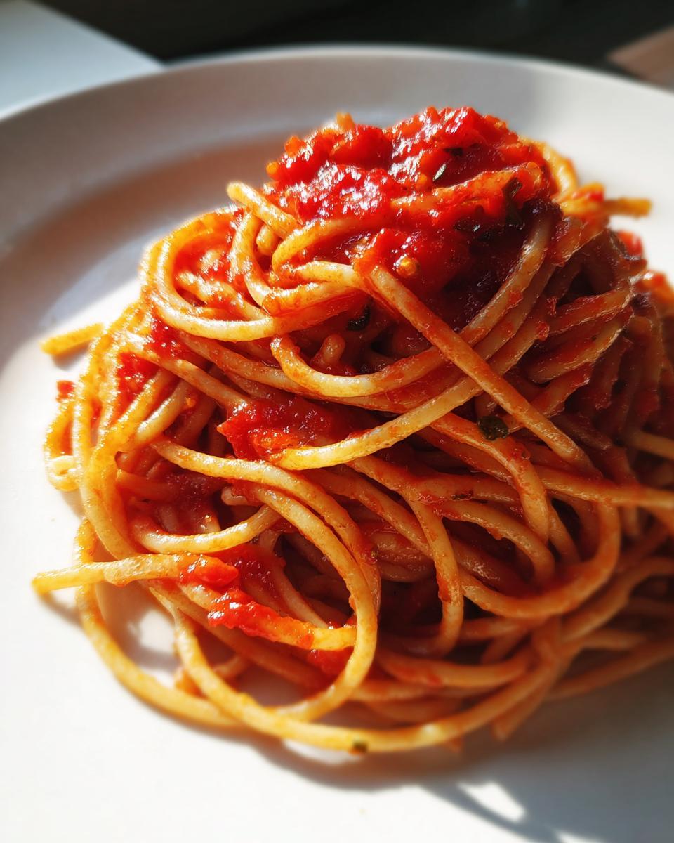 Plate of spaghetti pasta topped with rich red tomato sauce in natural light
