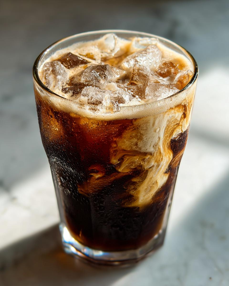 Glass of iced brown sugar shaken espresso recipe with ice cubes and swirls of cream