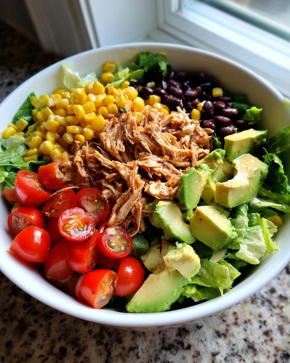 Bowl of chicken taco salad with corn, black beans, avocado, cherry tomatoes, and lettuce