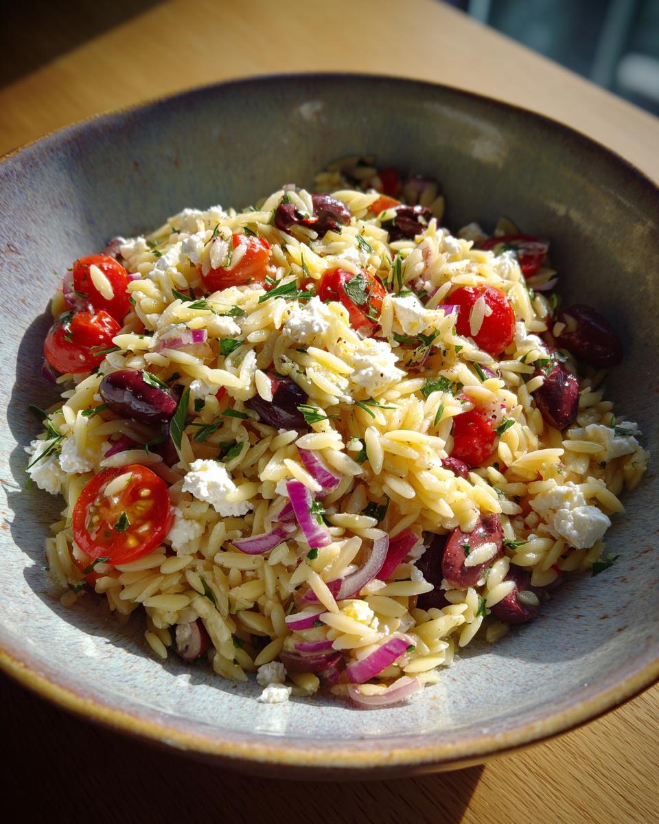 Bowl of orzo salad with feta, cherry tomatoes, red onions, olives, and herbs.