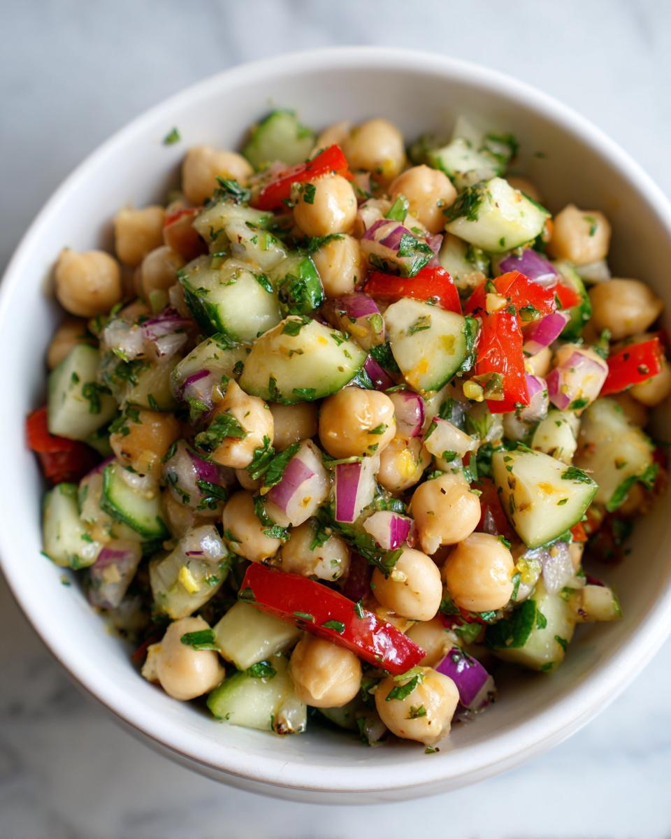 Close-up of a healthy chickpea salad with cucumbers, red onions, and red bell peppers in a white bowl