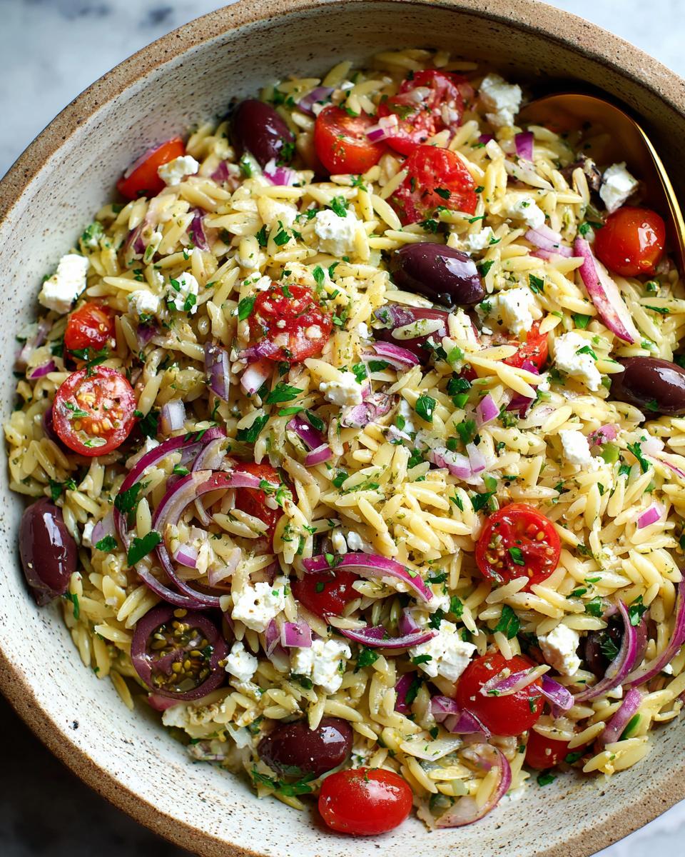 Bowl of orzo salad with feta, cherry tomatoes, red onions, olives, and herbs.