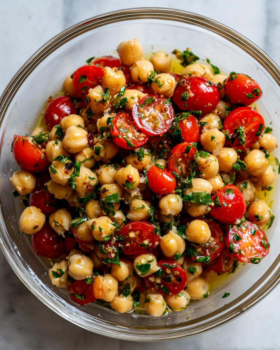 Bowl of quick chickpea salad with cherry tomatoes and fresh herbs dressed in olive oil.