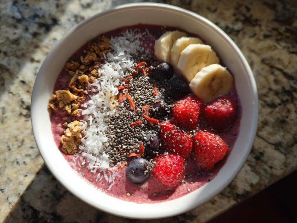 Simple smoothie bowl topped with banana slices, strawberries, blueberries, chia seeds, coconut flakes, and granola.